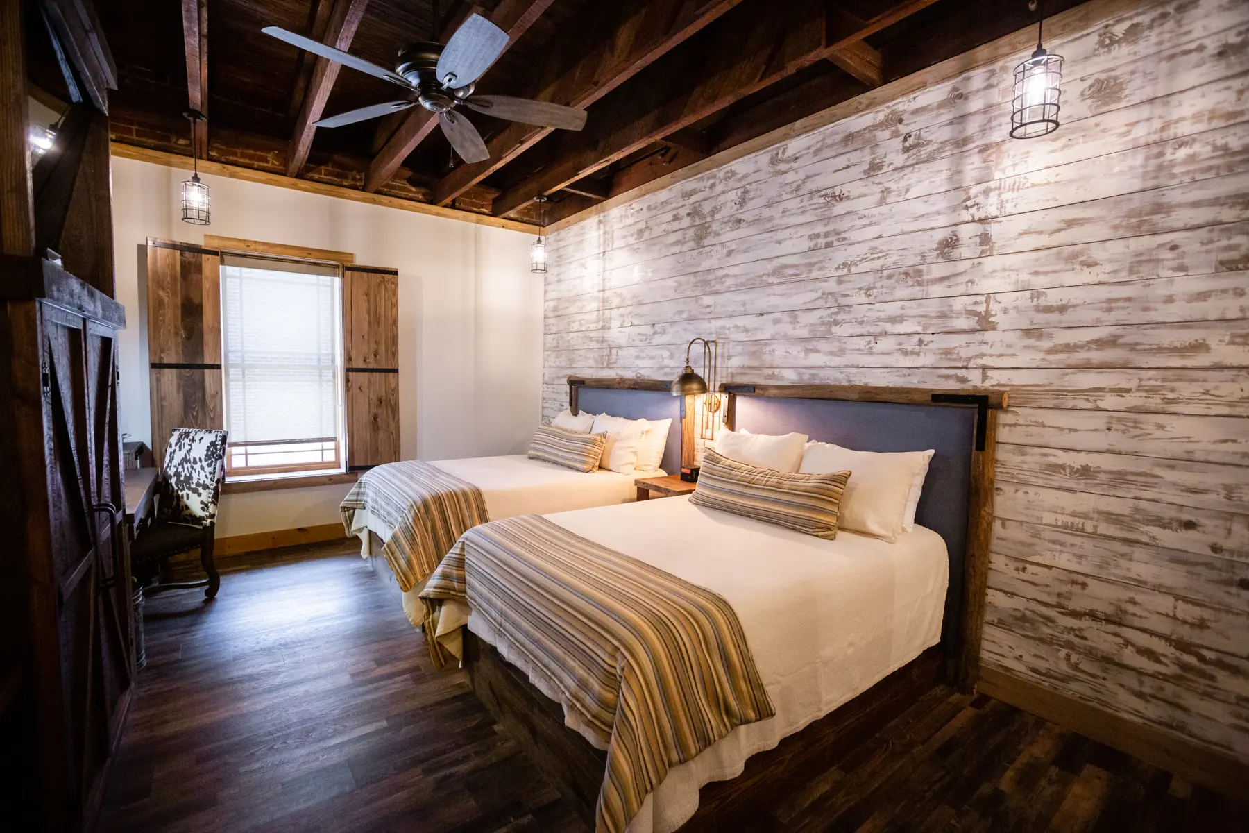 Cozy bedroom with two beds, exposed wooden beams, and rustic brick walls.